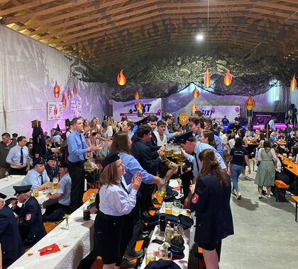 Feierndes Publikum steht auf Bierbänken in einer Festhalle