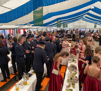 Jubelverein einer Feuerwehr feiert stehend auf Bierbänken in einem Bierzelt