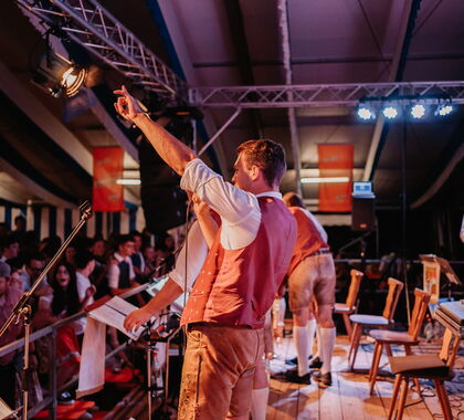 Die Musiker auf einer Bühne in einem Bierzelt vor feierndem Publikum