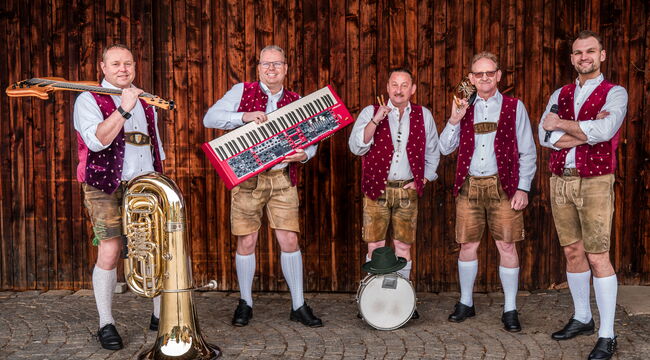 Fünf Musiker mit ihren Instrumenten vor einer dunklen Bretterwand