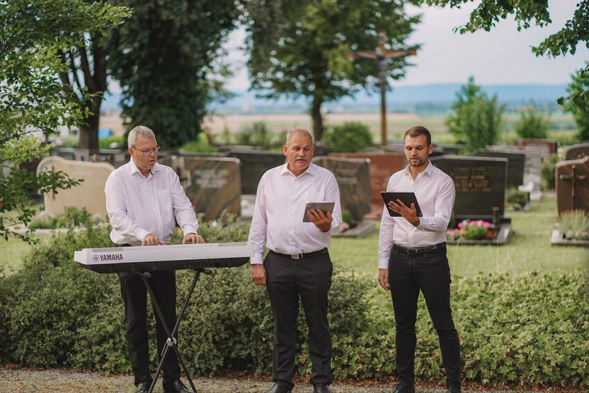 Drei Musiker vor Grabstätten auf einem Friedhof